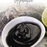 A close-up photo of a bowl of oyster sauce, an oyster shell, and a lime on a wooden table.