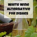 A bottle of white wine beside a basket of white grapes.