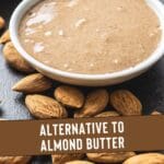 A photo of a bowl of almond butter and a pile of almonds on a wooden table.