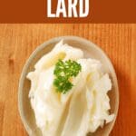 A close-up photo of a round white bowl filled with lard on a brown wooden table.