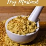 A close-up view of a rustic wooden table holding a bowl of bright yellow dry mustard and a traditional mortar and pestle.
