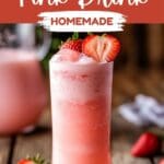 A homemade Pink Drink in a glass with ice, surrounded by fresh strawberries.