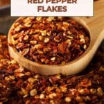 A wooden spoon overflowing with red pepper flakes.