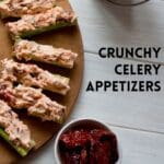 Crunchy celery appetizers with sun dried tomatoes on a wooden cutting board.