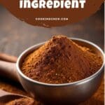 A close-up photo of a bowl filled with ground cinnamon powder next to several cinnamon sticks on a wooden table.