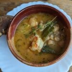 Close up of a brown bowl with shrimp, beans, lemony broth and leeks