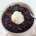 A small ramekin or mug with a warm, gooey chocolate lava cake, with a spoon digging into the center.