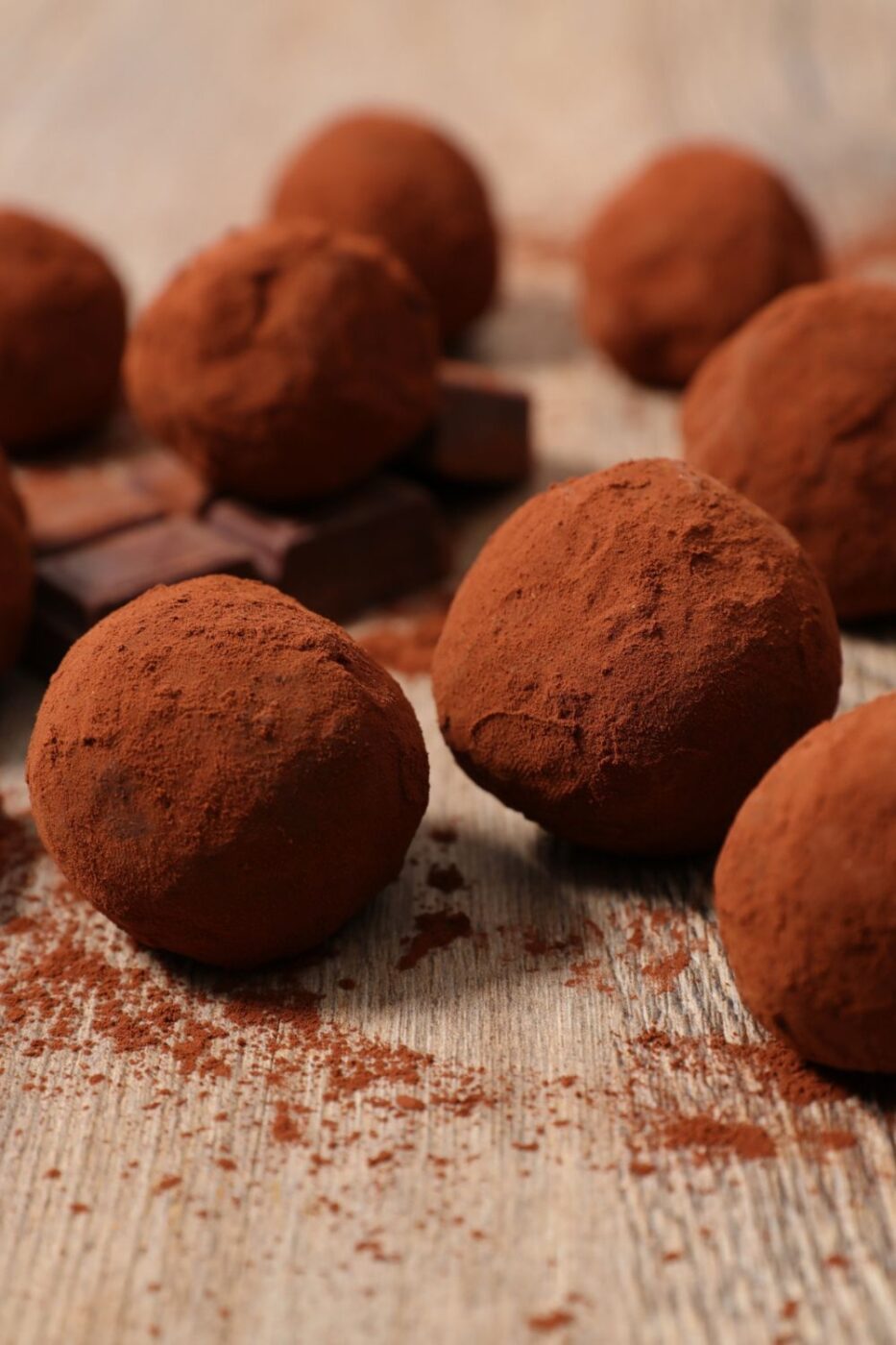 A small pile of rich, dark vegan chocolate truffles, some dusted with cocoa powder, some with sprinkles.