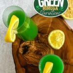 Two green mimosa drinks in glasses on a wooden cutting board.