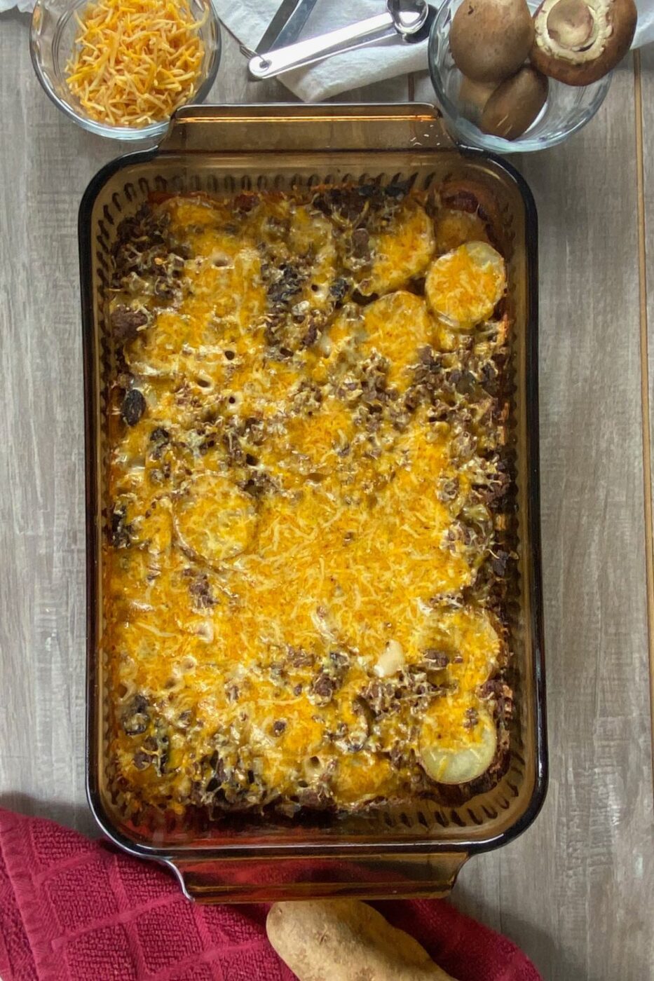 A baking dish filled with a golden-brown ground beef and potato casserole, topped with melted cheese.