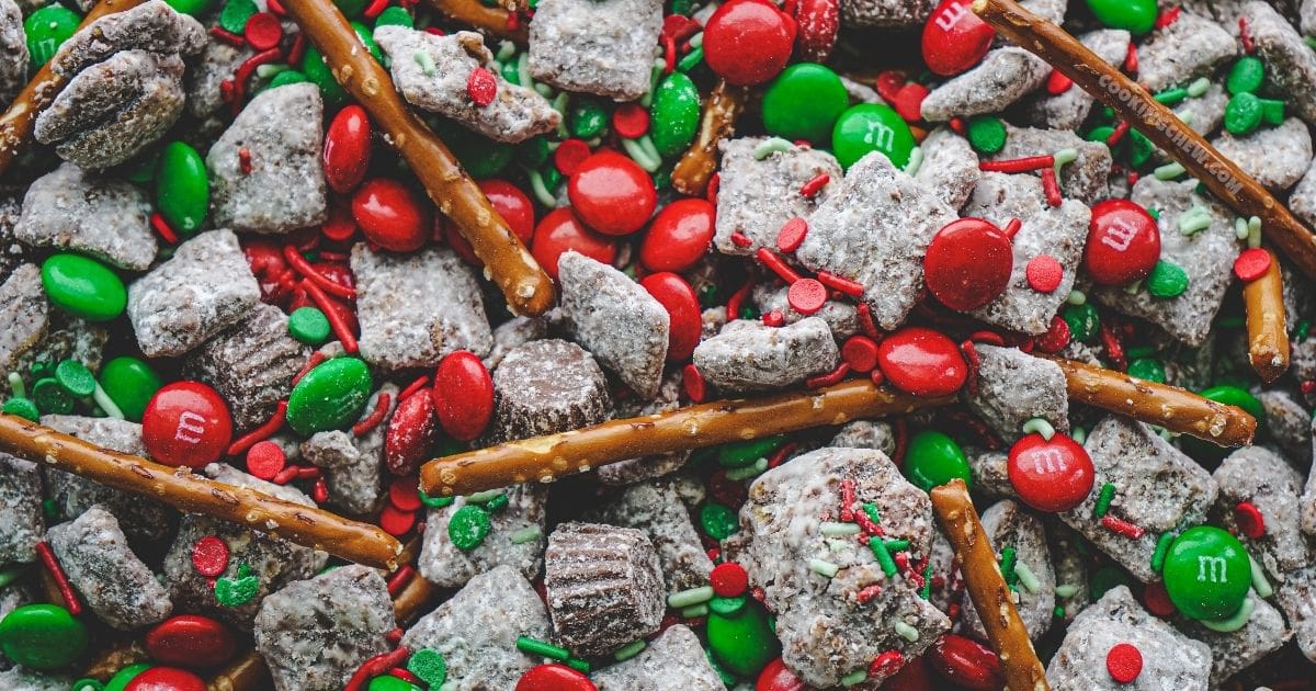 A bowl of red and green puppy chow, made with Chex cereal, peanut butter, powdered sugar, and festive sprinkles.