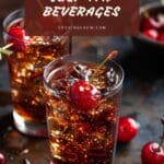 A cherry cola cocktail glass filled with ice and a cherry on top sits on a wooden table.