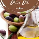 A bottle sits on a table next to a bowl of green olives.