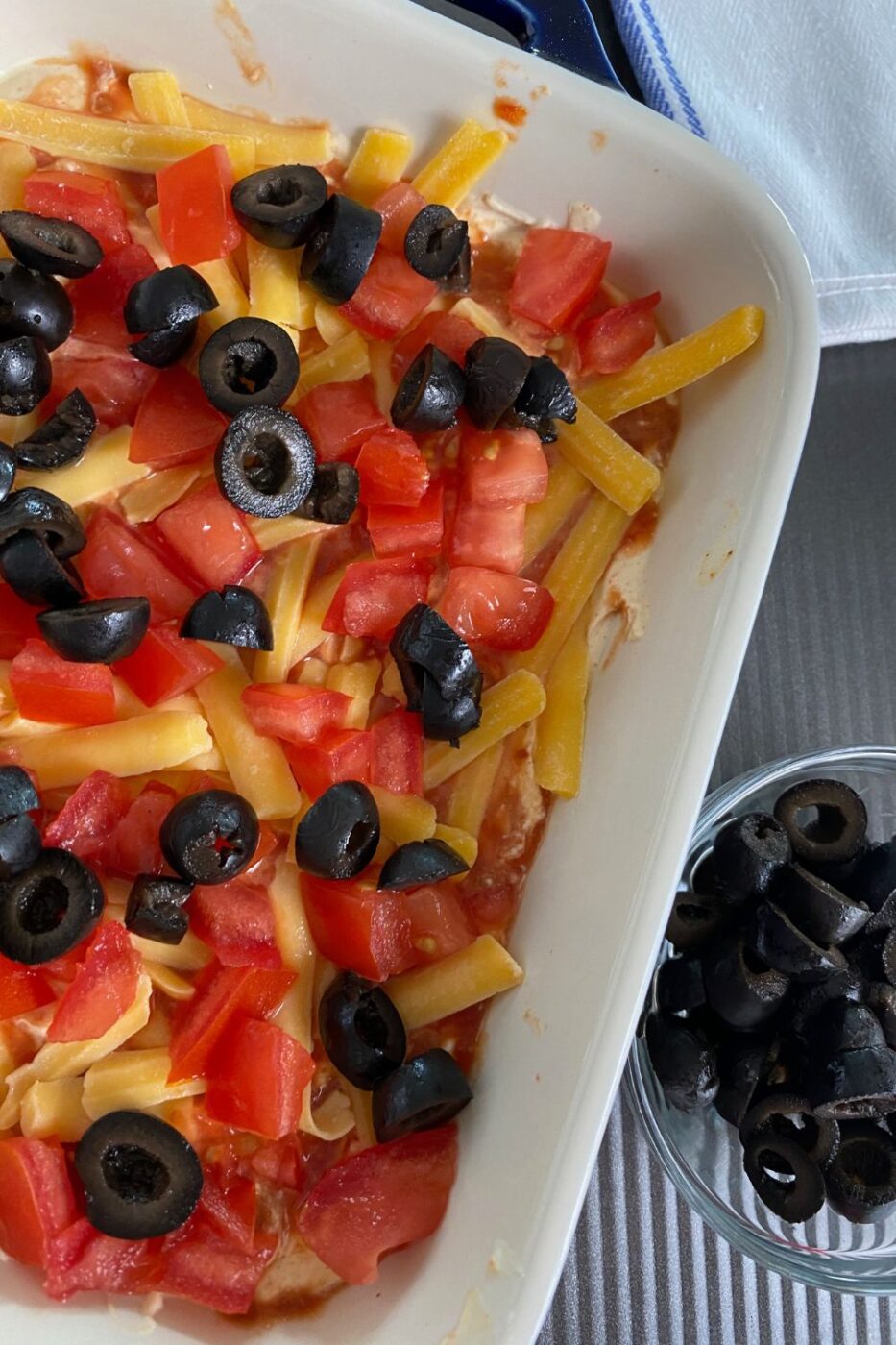 A vibrant layered taco dip with cheese, tomatoes, and black olives, surrounded by tortilla chips.