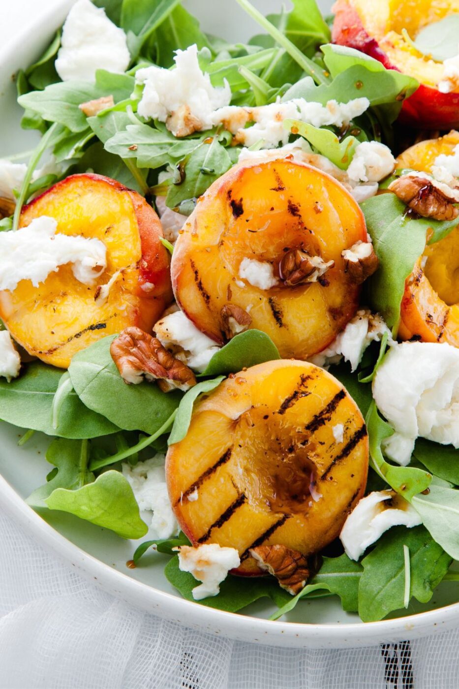 A vibrant bowl of grilled peach salad with mixed greens, cheese, and a light dressing.