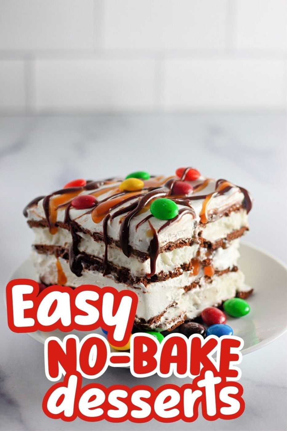 A layered slice of cake made with vanilla ice cream sandwiches, cool whip, M&Ms, and sundae fudge topping