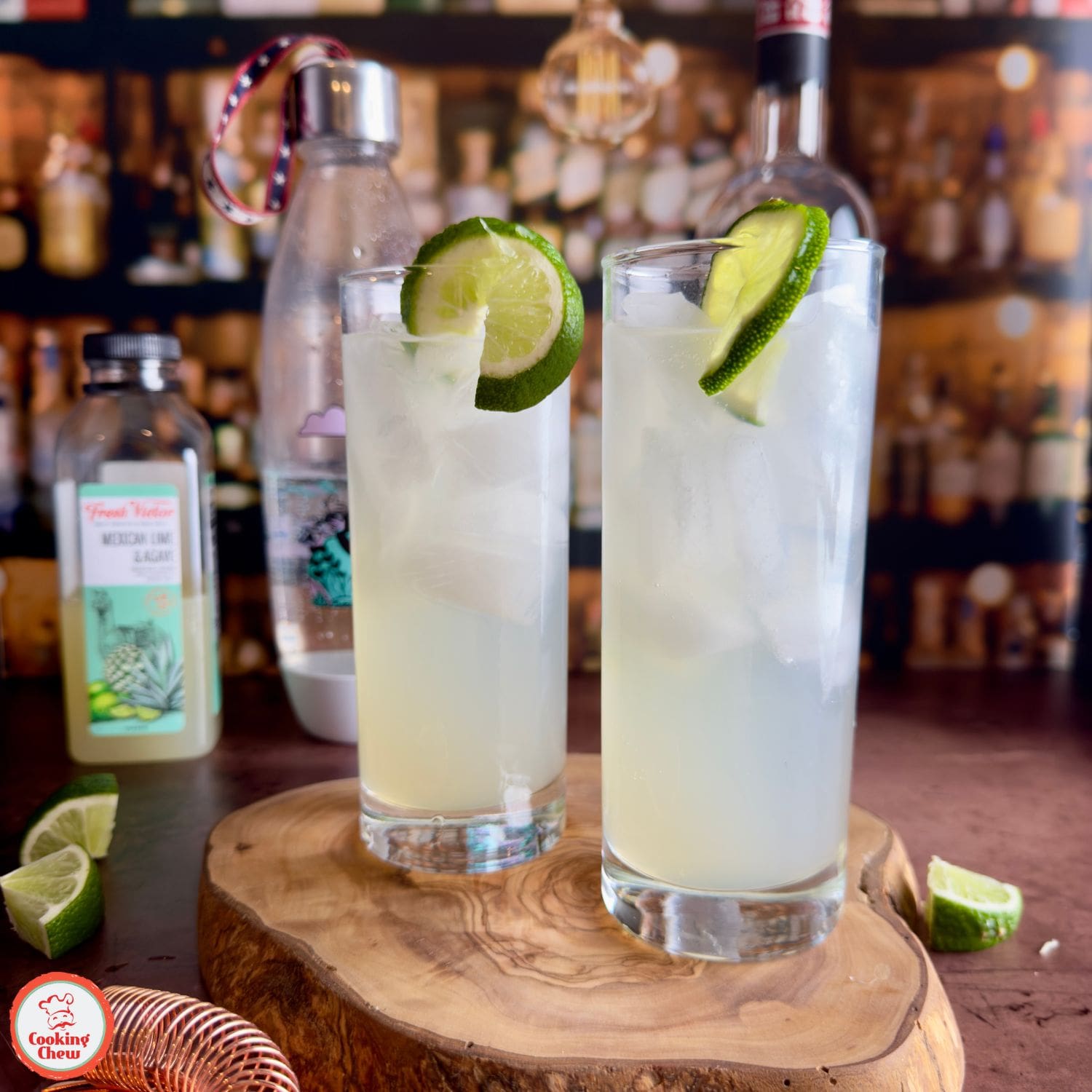 A glass of vodka lime cooler on a wooden table with fresh lime wedges.