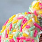A stack of soft cream cheese sprinkle cookies, topped with colorful rainbow sprinkles.