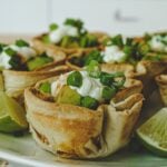 Golden-brown baked taco cups filled with seasoned ground beef, cheese, lettuce, and tomato.