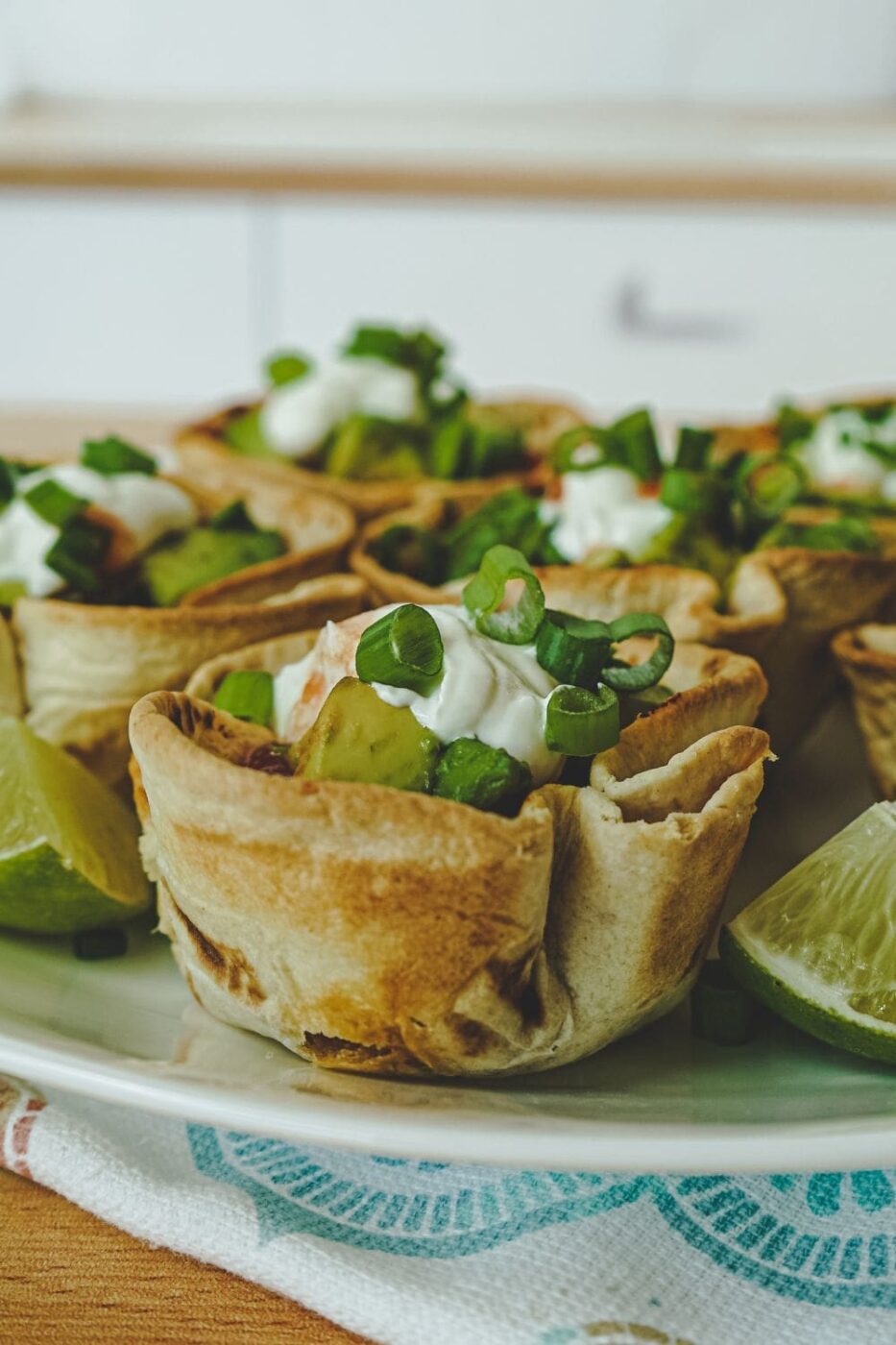 Golden-brown baked taco cups filled with seasoned ground beef, cheese, lettuce, and tomato.