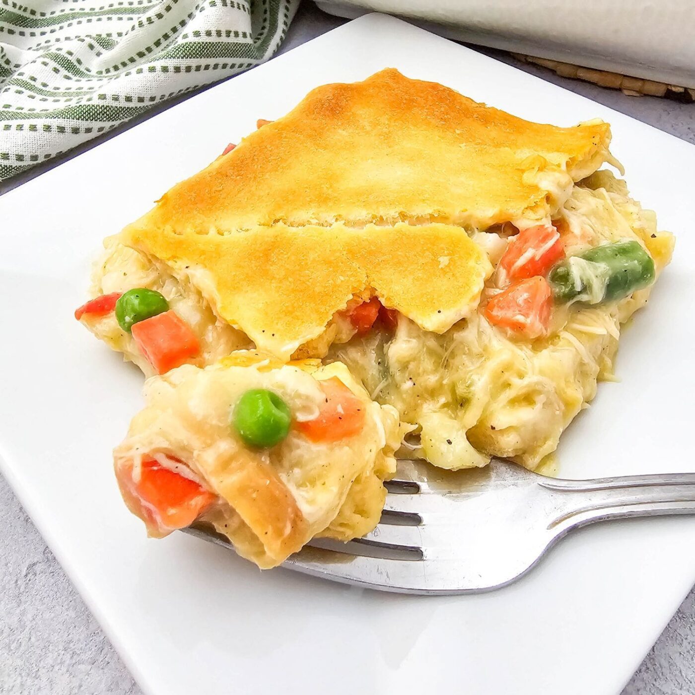 Chicken pot pie casserole with golden crescent roll topping served on a white plate.