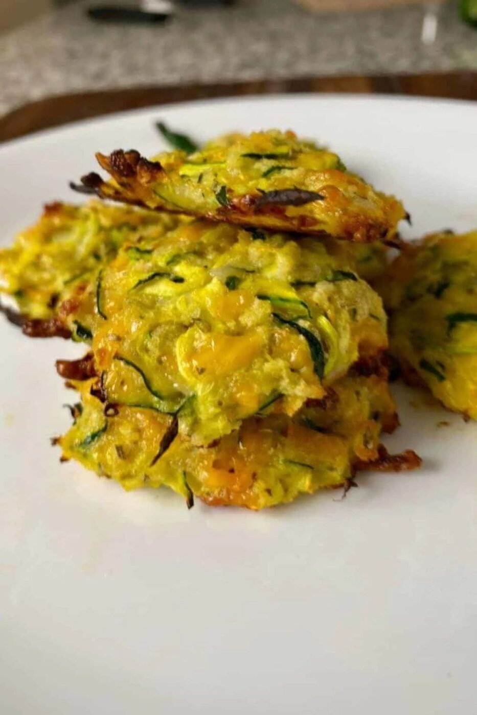 Stack of zucchini fritters with shredded cheese and herbs.