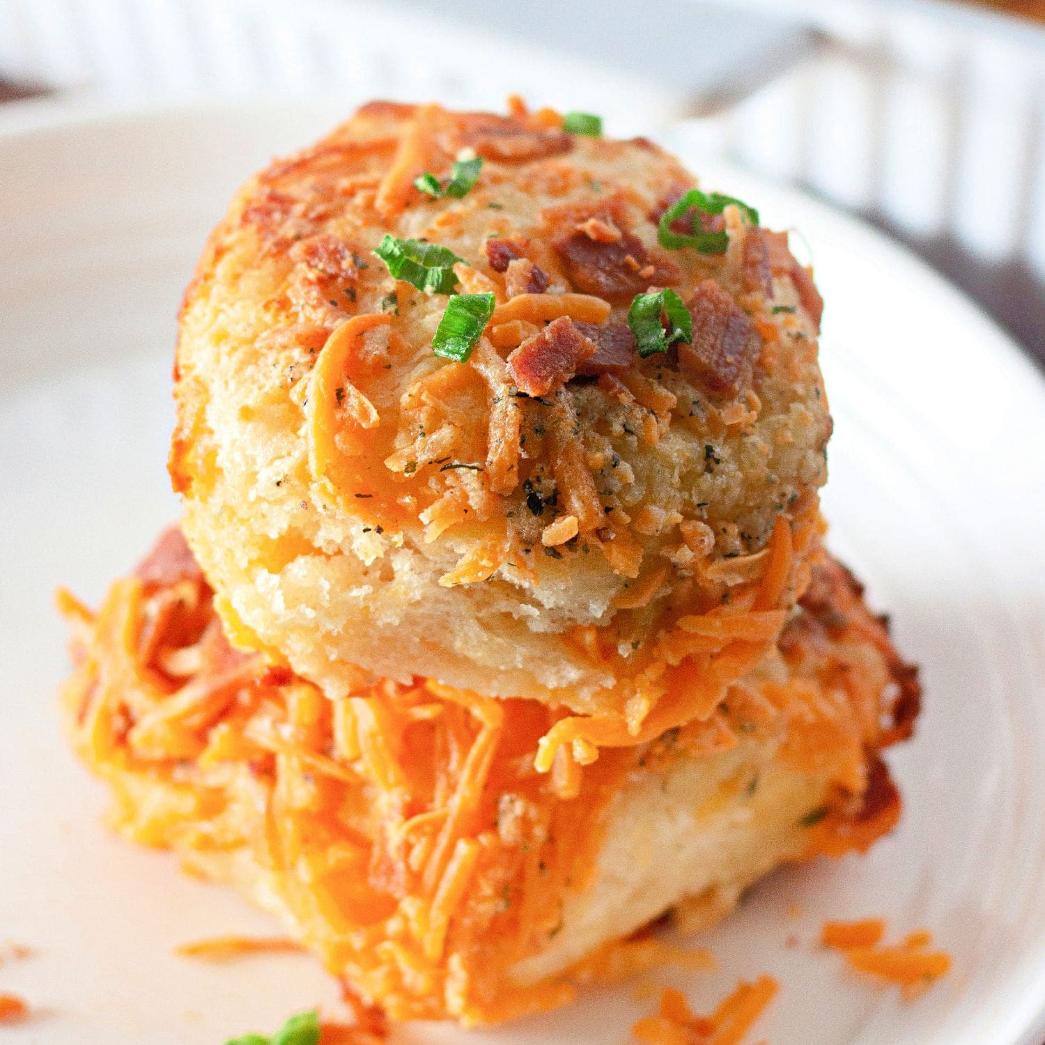 Stacked biscuits topped with melted cheddar and bacon on a plate.