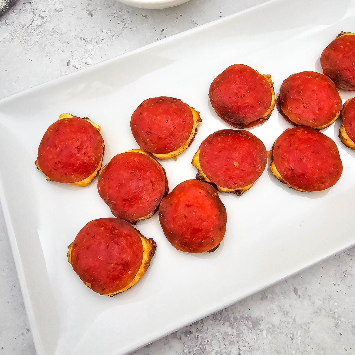 Baked pepperoni and cheese bites arranged on a white serving platter.