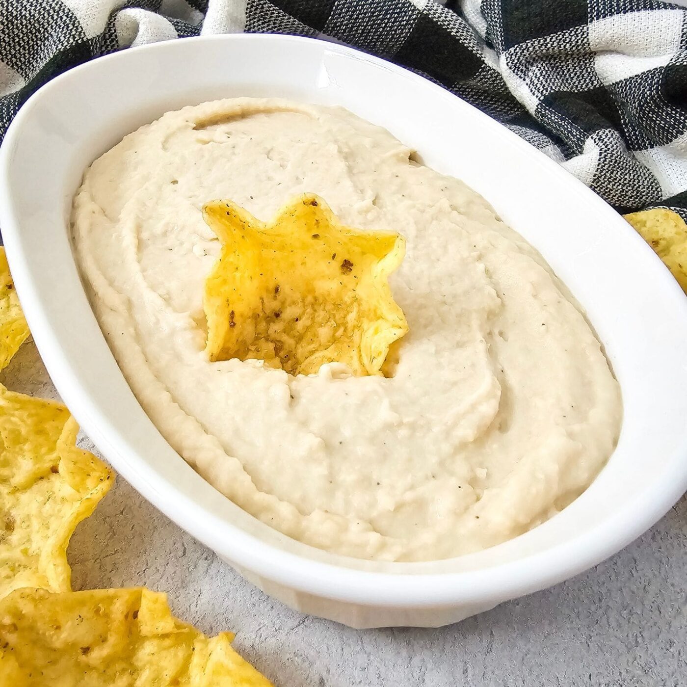 Creamy white bean dip in oval bowl with a chip dipped in the center.