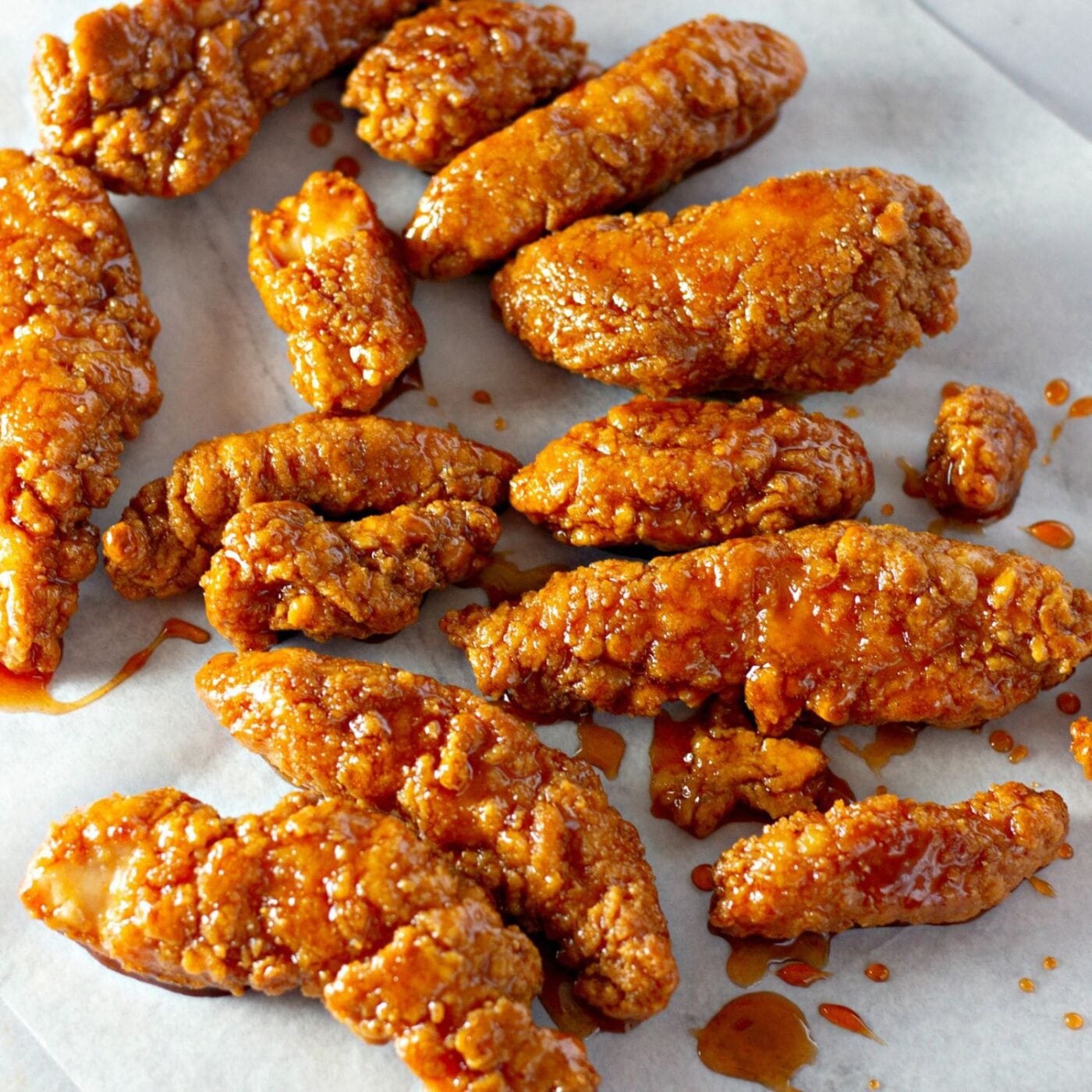 Chicken tenders with sticky glaze dripping on parchment paper