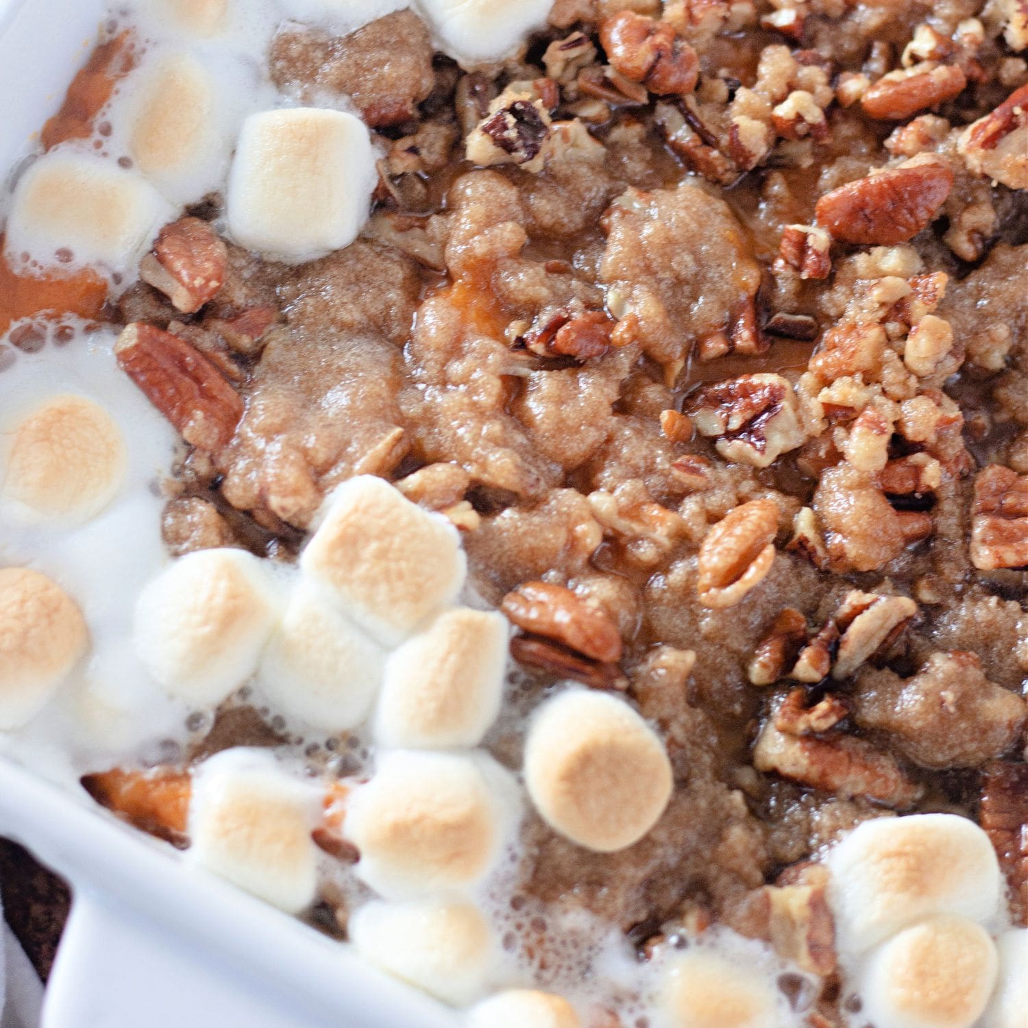 Sweet potato casserole topped with marshmallows and pecans in a white baking dish.