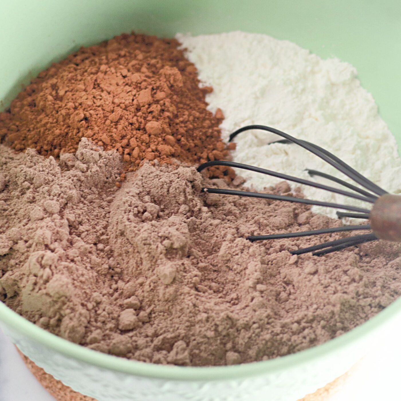 Dry cake mixes and cocoa powser with a whisk in a bowl