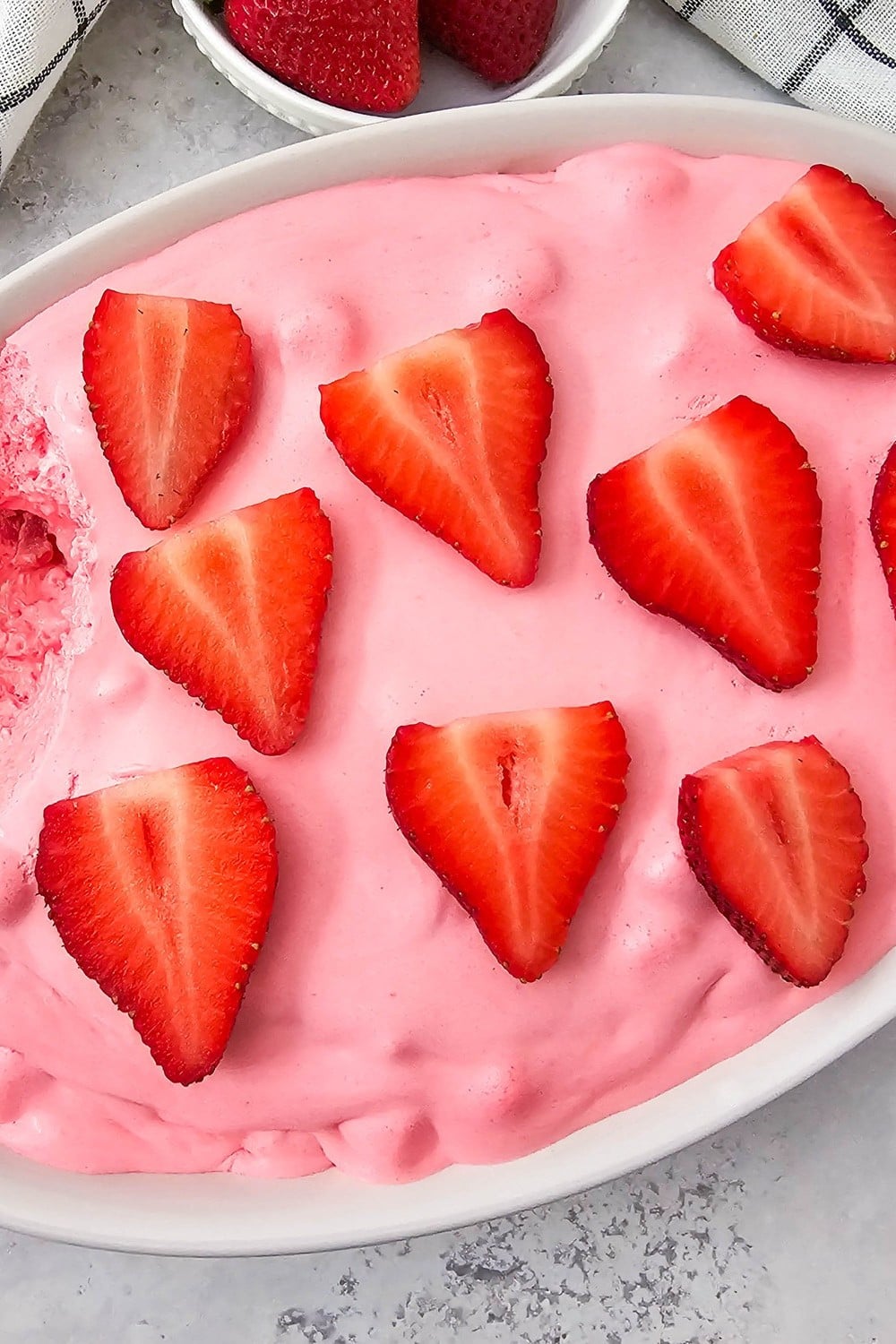 A bowl of pink fluff with fresh strawberries on top.