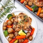 Close overhead of plated honey glazed pork chop with roasted potatoes, carrots, and zucchini, garnished with thyme