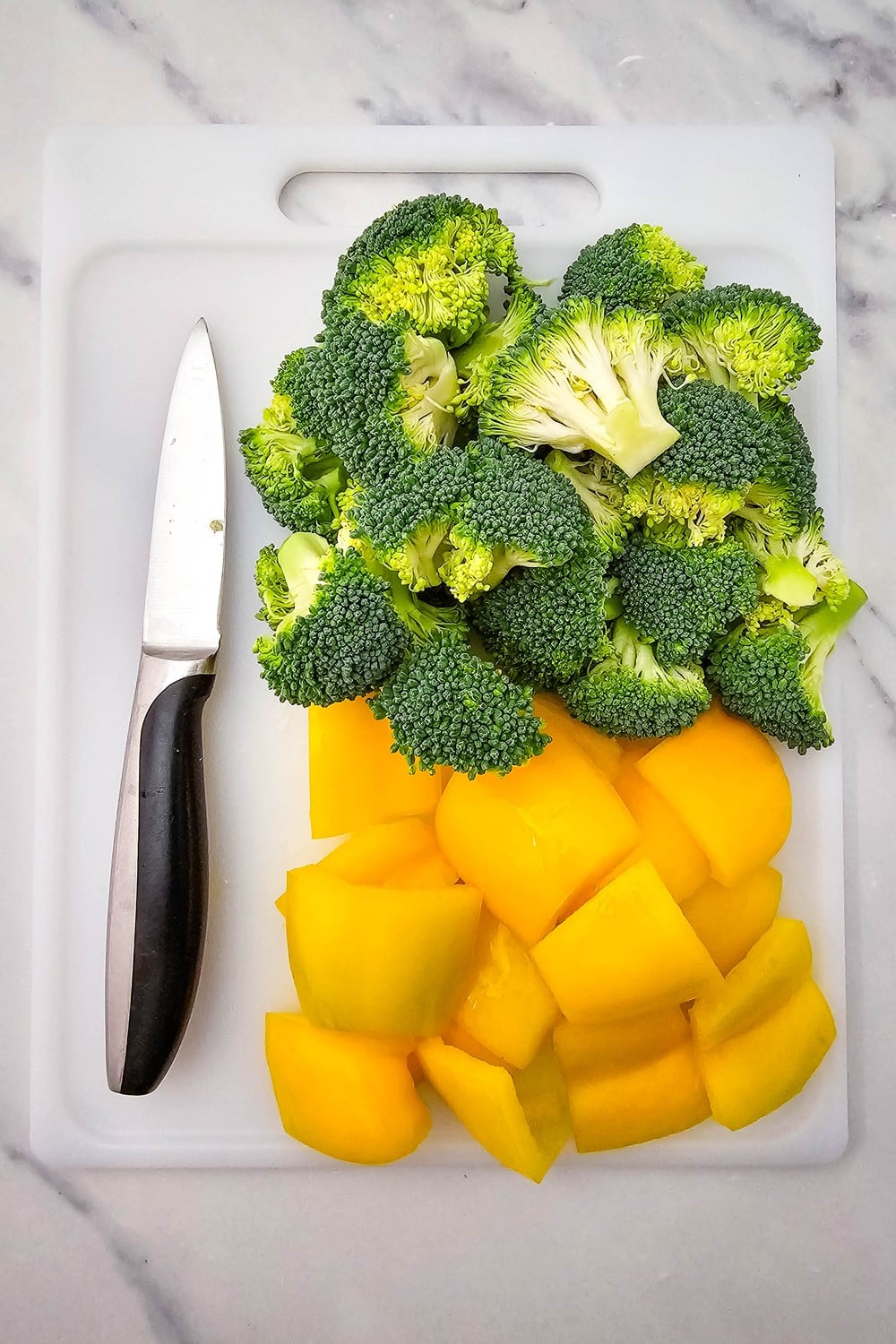 Chopped broccoli florets and yellow bell pepper pieces on a cutting board
