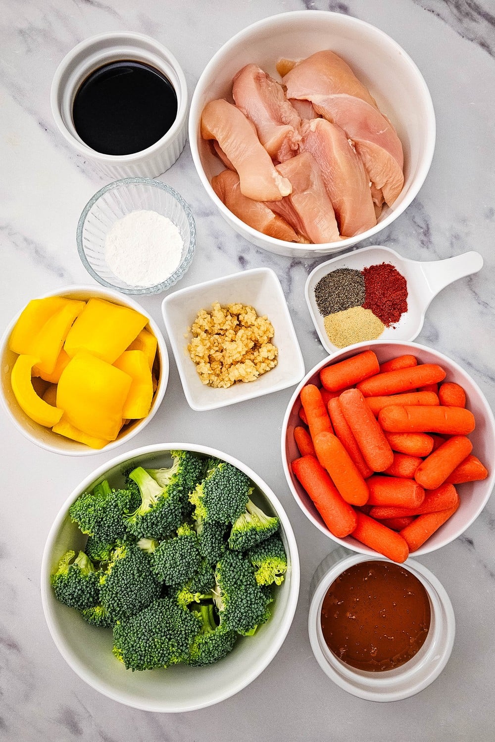 Sheet pan honey garlic chicken ingredients including chicken breasts, broccoli, baby carrots, yellow bell pepper, soy sauce, honey, garlic, and spices