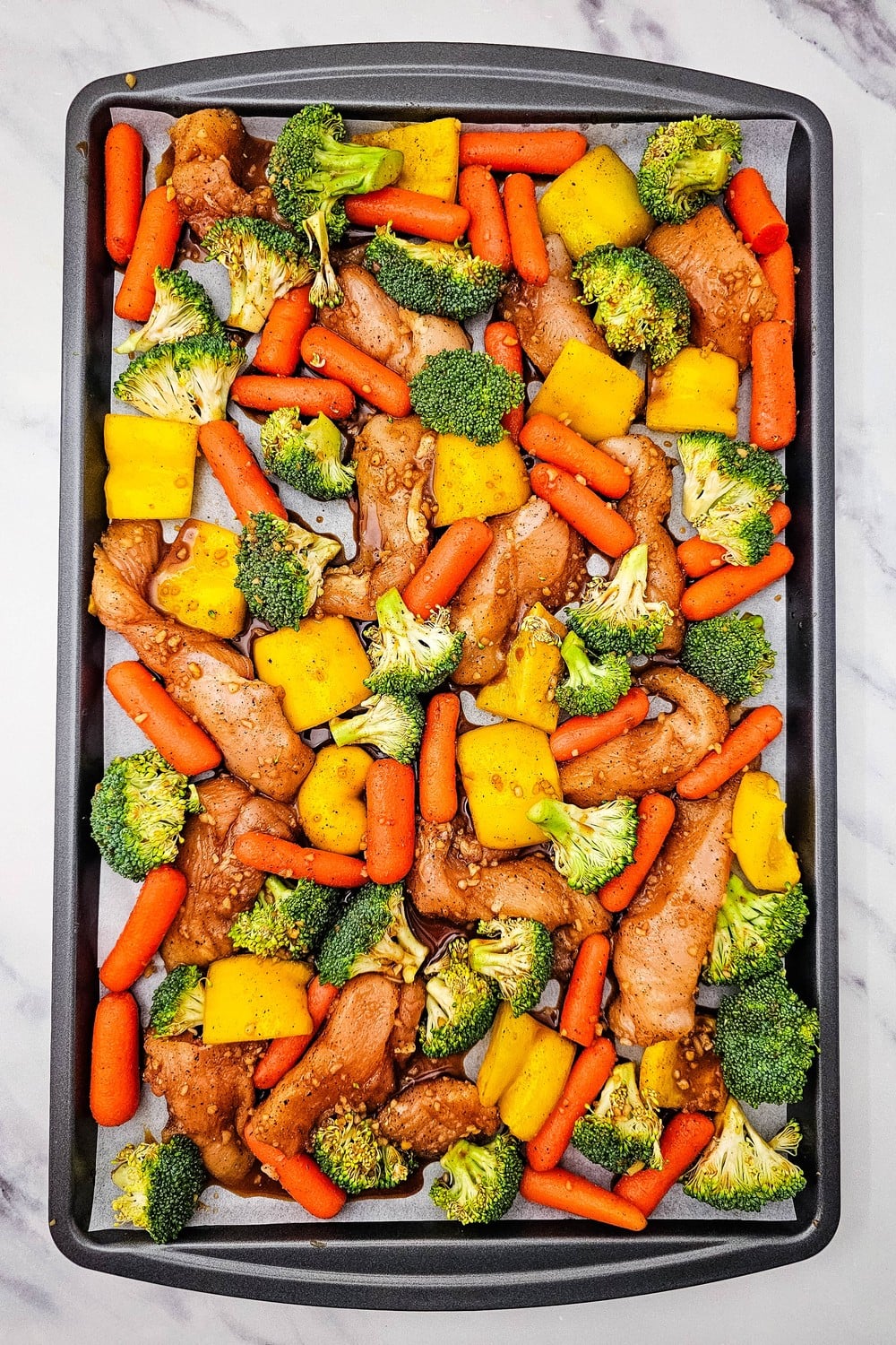 Honey garlic chicken and vegetables spread in a single layer on a sheet pan ready to bake