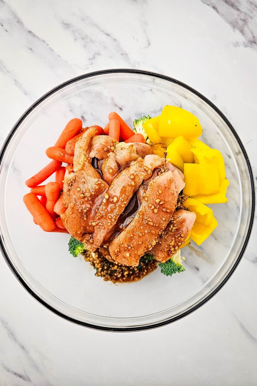 Honey garlic sauce poured over raw chicken and vegetables in a glass bowl