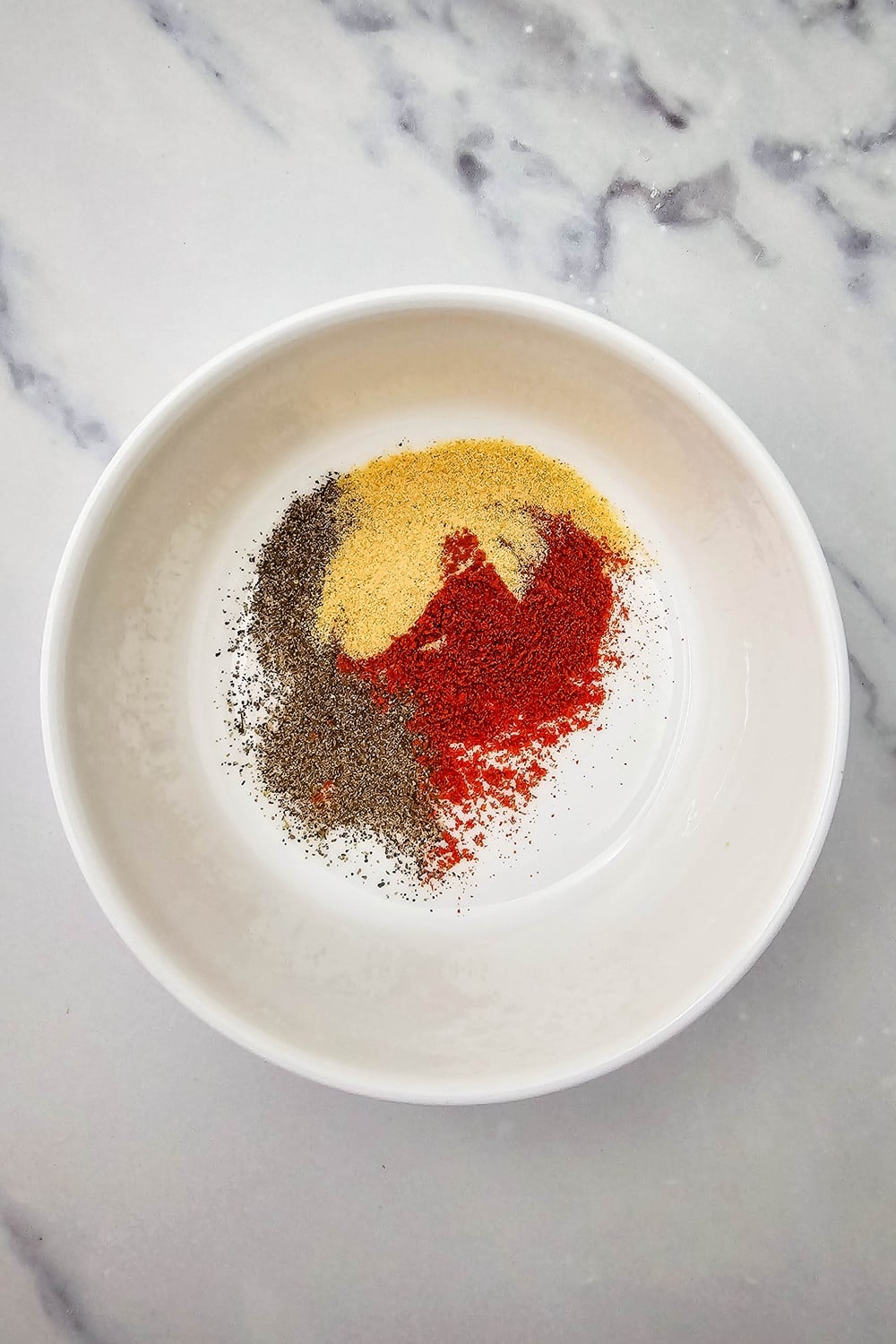 Dry spice blend with garlic powder, paprika, and black pepper in a white bowl