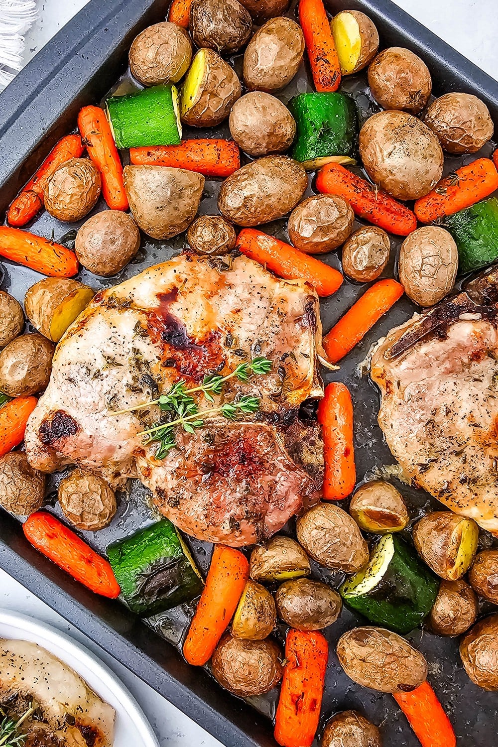 Direct overhead of finished sheet pan honey glazed pork chops with roasted vegetables and fresh thyme