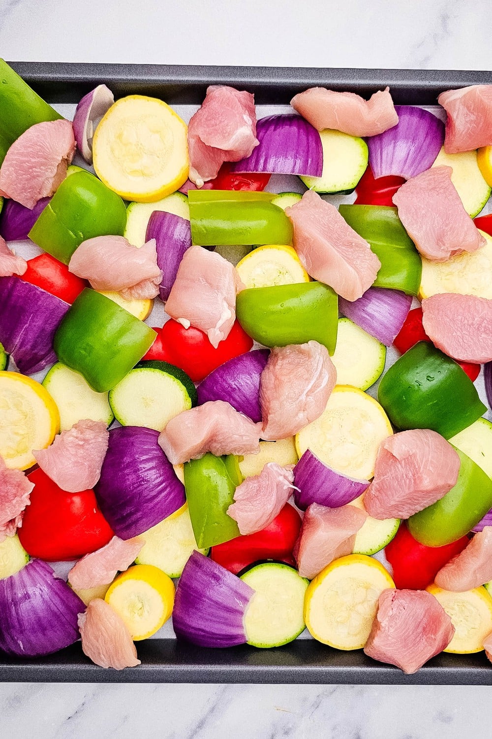Raw chicken and vegetables spread in single layer on sheet pan