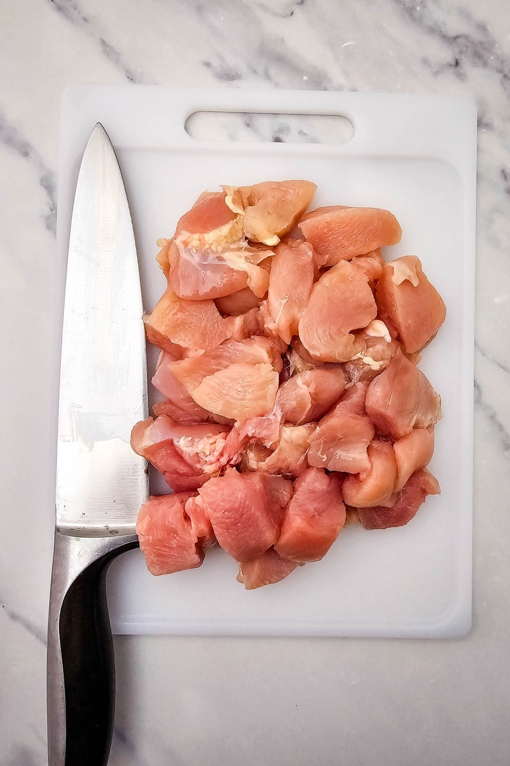 Cubed raw chicken breast pieces on white cutting board
