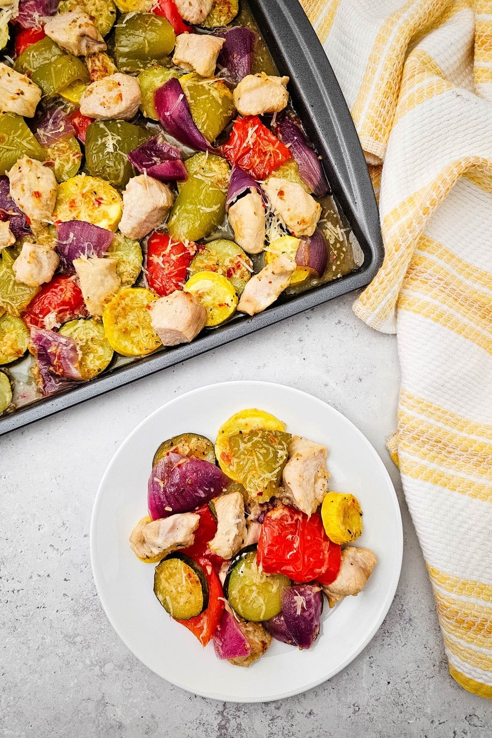Plated serving of sheet pan Italian chicken and veggies with full pan alongside