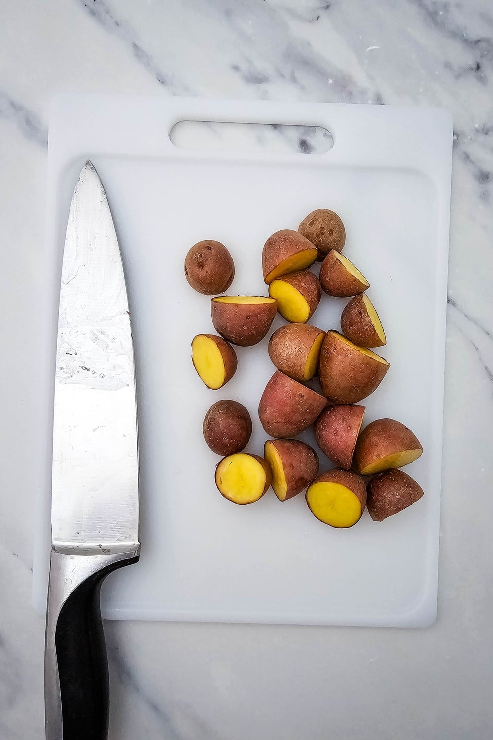 Halved baby red potatoes on white cutting board with chef's knife