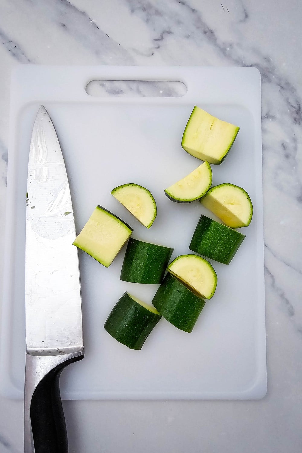Zucchini cut into 2-inch pieces on white cutting board with chef's knife