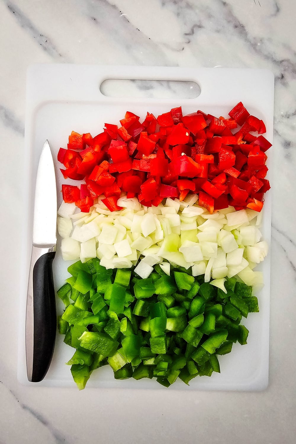 Diced red bell pepper, onion, and green bell pepper on a cutting board