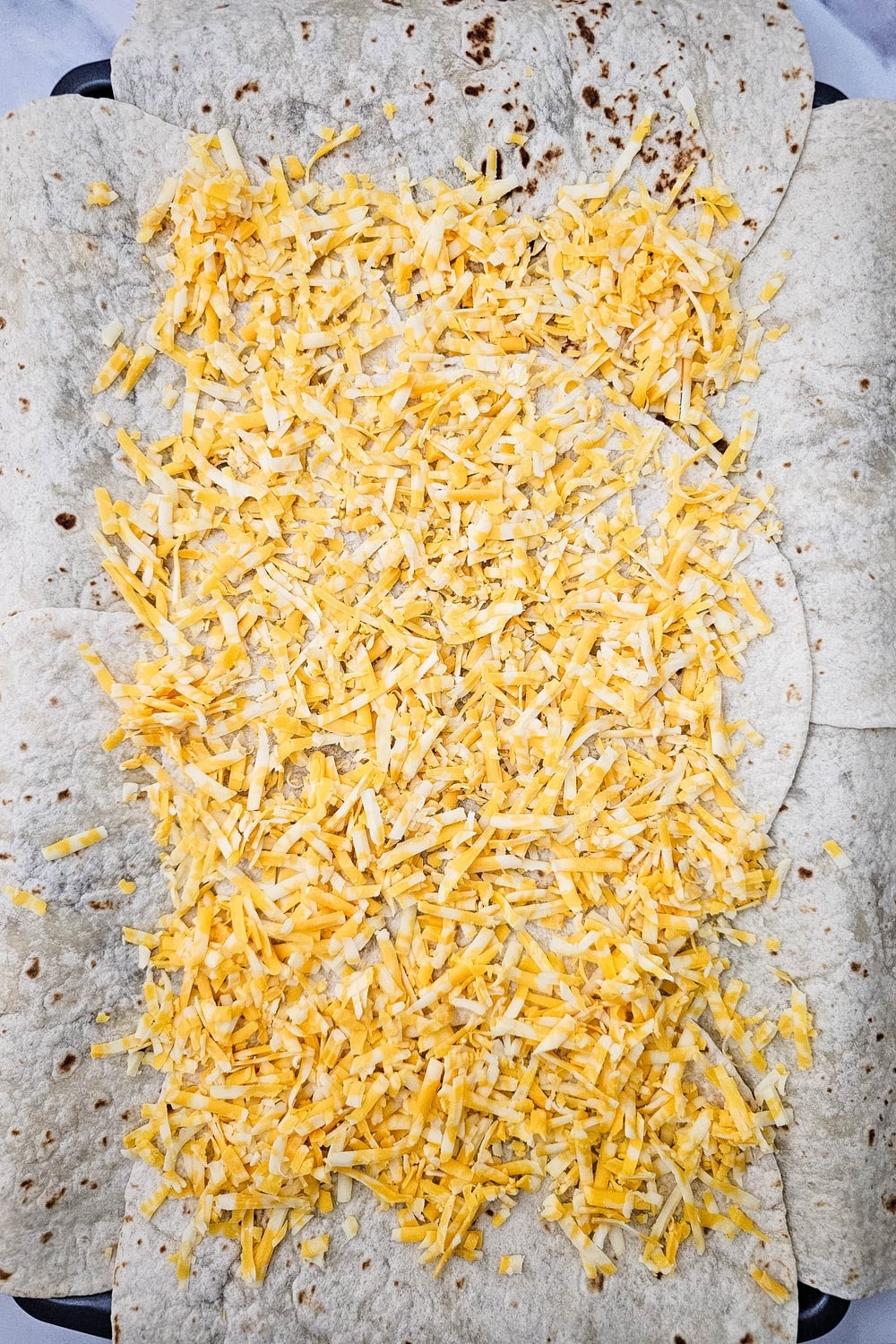 Shredded colby jack cheese sprinkled over tortillas on the sheet pan