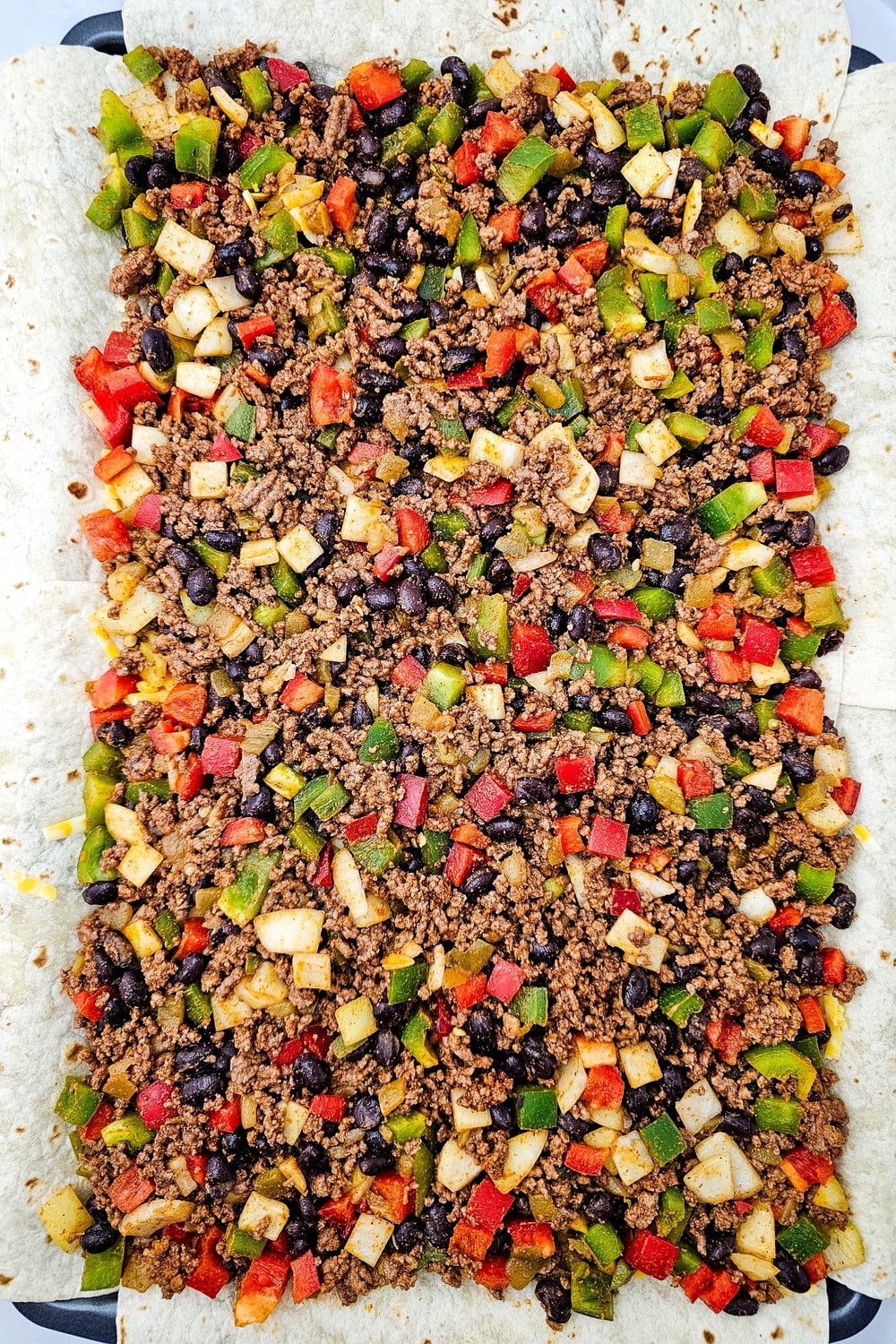 Beef and vegetable mixture spread over the cheese layer on the sheet pan