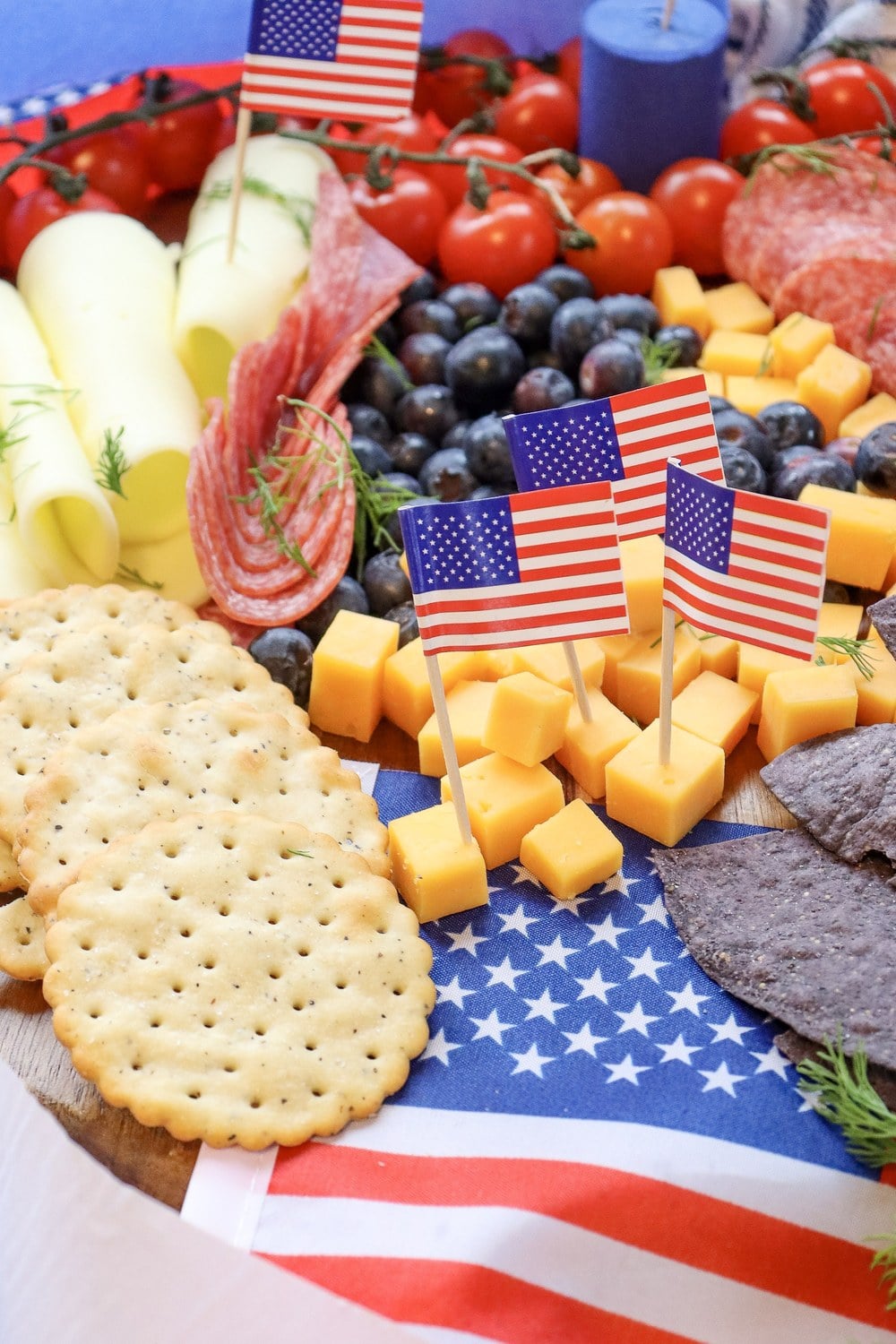 Angled view of a finished 4th of July charcuterie board with American flag picks, blue corn chips, blueberries, cheddar cubes, and ranch dip
