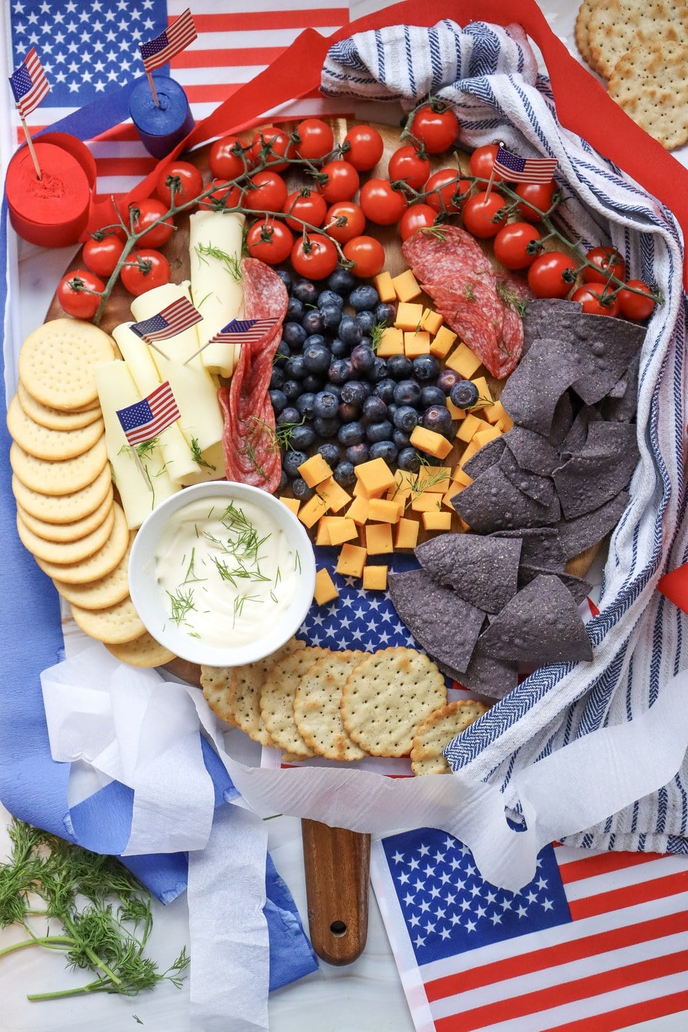 Finished 4th of July charcuterie board overhead with cherry tomatoes, swiss cheese with mini American flag picks, salami, blueberries, cheddar, blue corn chips, and ranch dip
